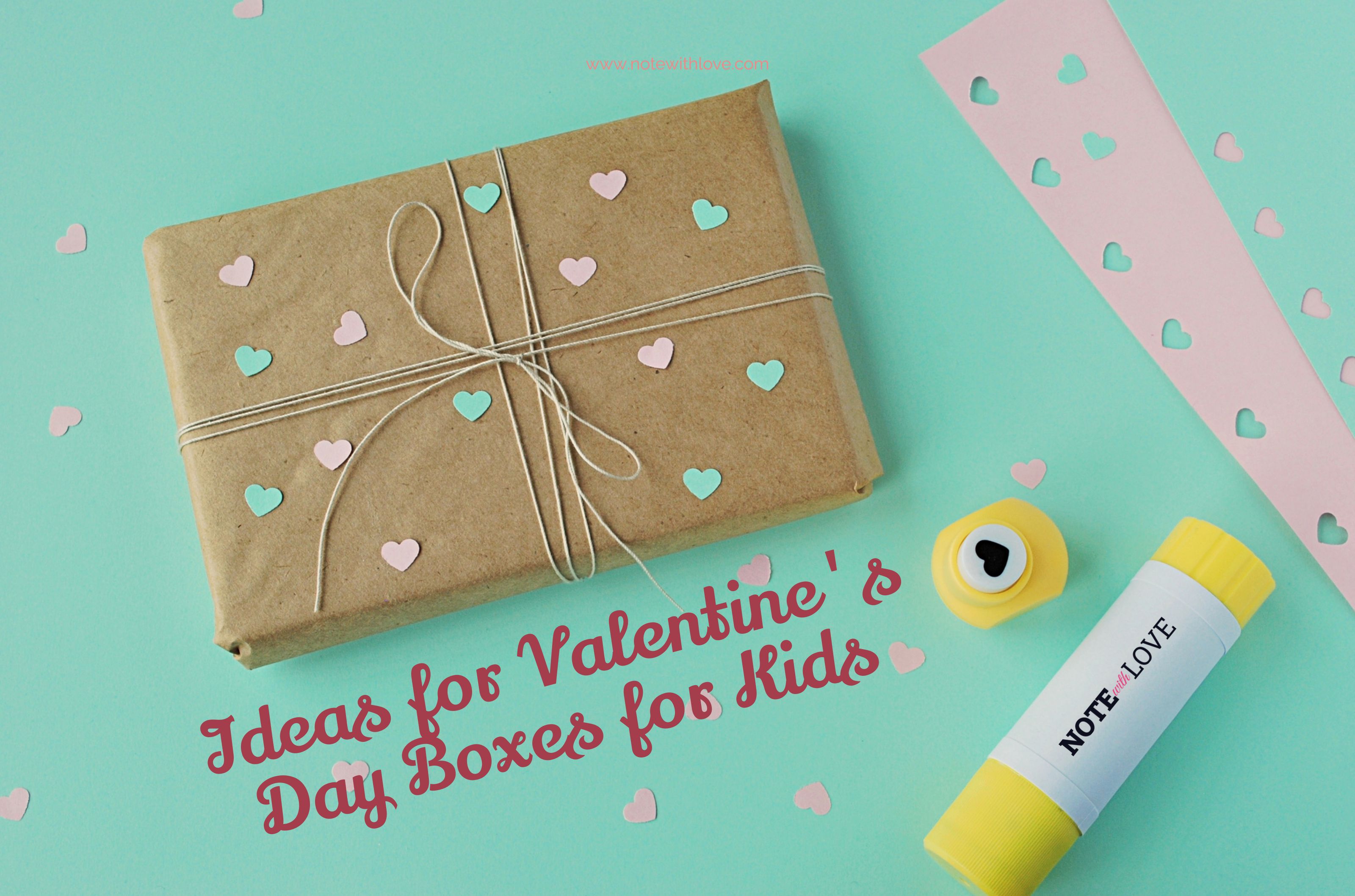 A box wrapped in brown paper and decorated with pink and light green shaped paper hearts. Beside it, there are other things for crafting.