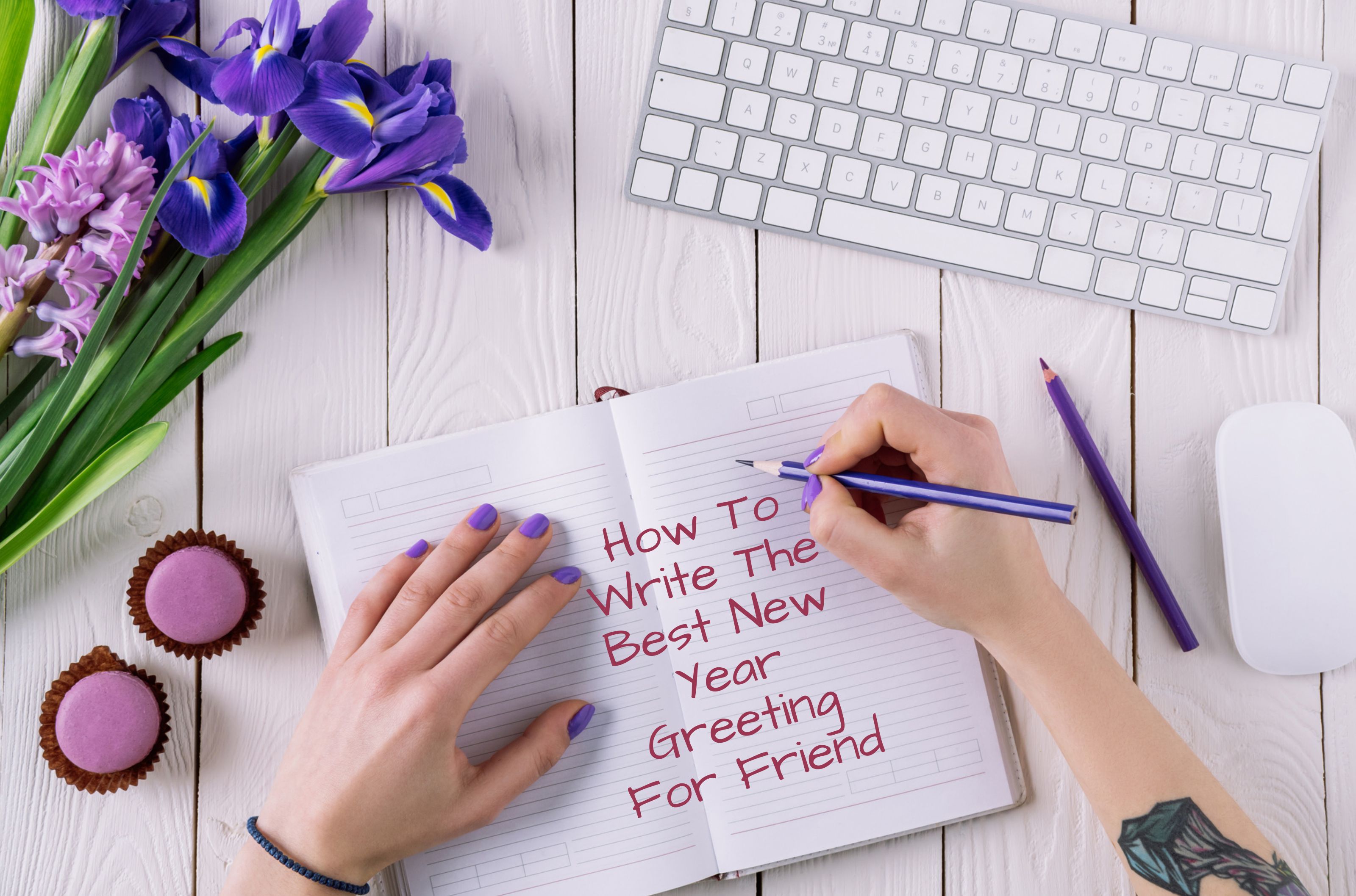 A person with purple nail paint writing on a diary with pencil. It is on a white table. On the table there are white keyboard and mouse, two small pink cupcakes, and purple and pink flowers.