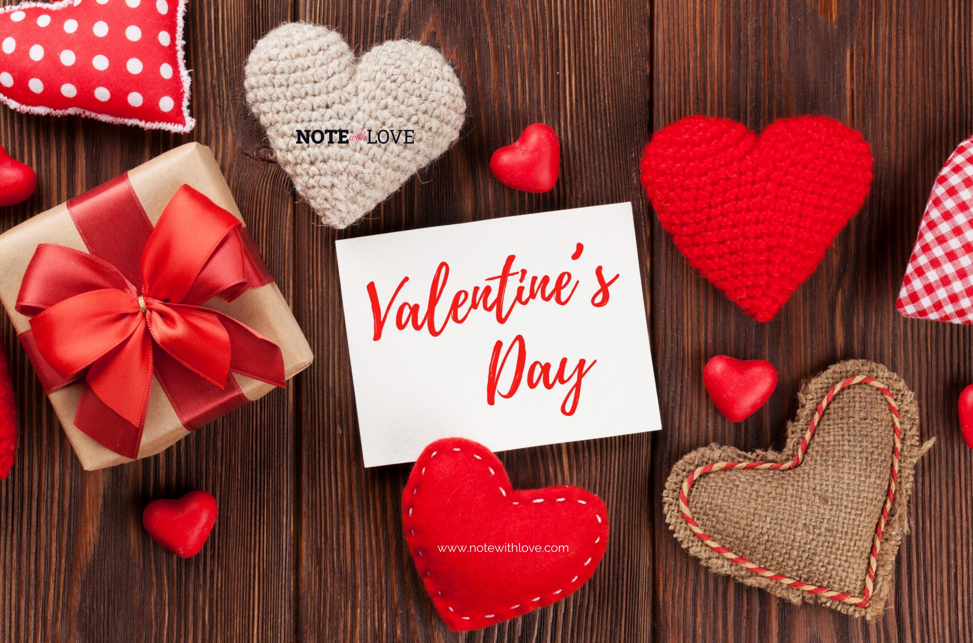 Heart shaped cushions of red color, plaid cloth and sack kept on a wooden surface along with a gift with red bow and a note with Valentine's Day written on it.