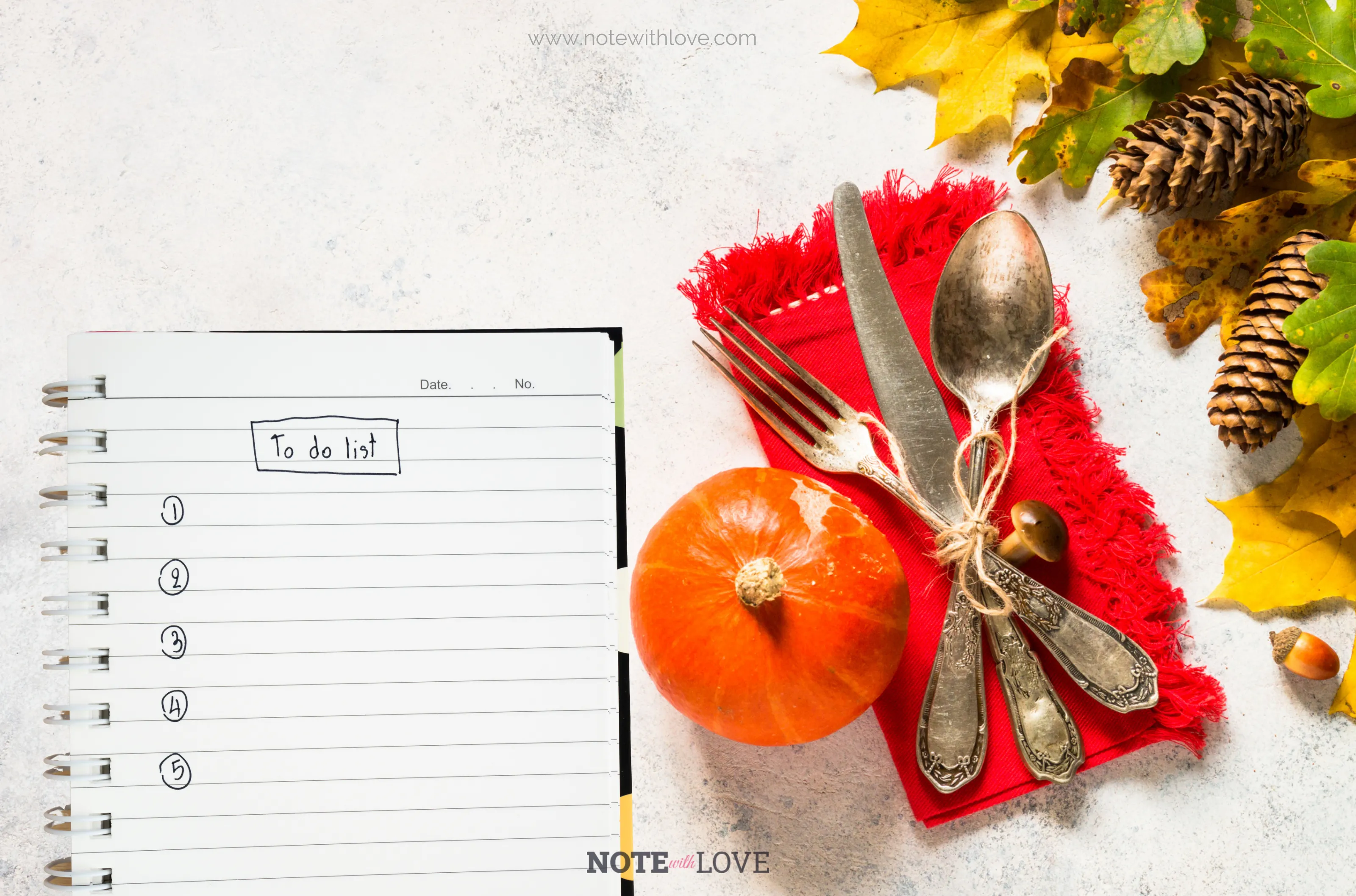 A diary with an empty to-do list kept on a surface. a decorative small pumpkin, other fall decors and cutlery is placed beside it.